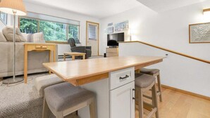 Un espacio habitable compacto con kitchenette, comedor, sofá y ventana con vista a vegetación.