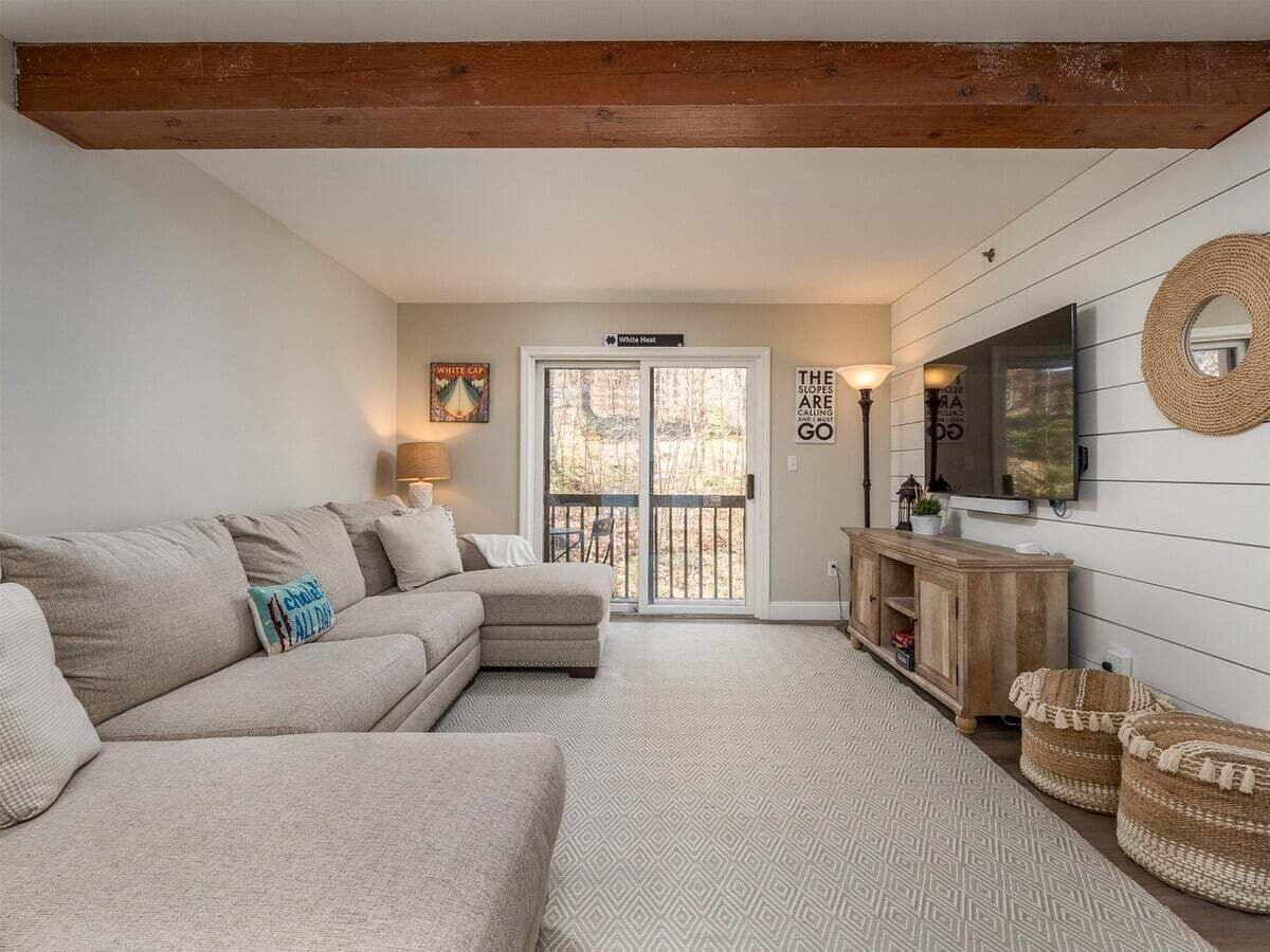 A cozy living room with a sectional sofa, a wooden TV stand, and a sliding glass door leading to an outdoor area.