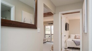 Un pasillo que conduce a un dormitorio con una cama, un ventanal y una puerta.