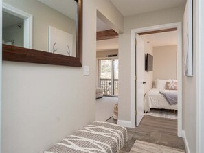 A hallway leading to a bedroom with a bed, a window, and a door.