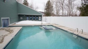 Una piscina rectangular con una escalera en un lateral, una valla blanca y un edificio de fachada verde al fondo.