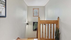 A hallway with a wooden chair, a small window, and a framed picture on the wall.