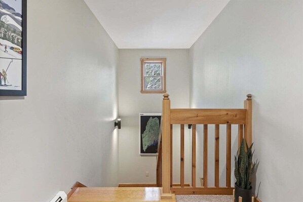 A hallway with a wooden chair, a small window, and a framed picture on the wall.