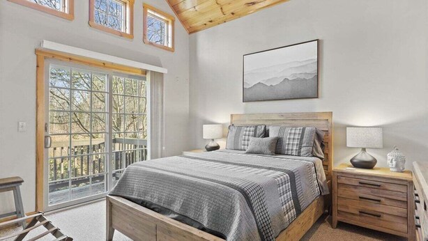 A bedroom with a large window, a bed, a nightstand, and a painting on the wall.