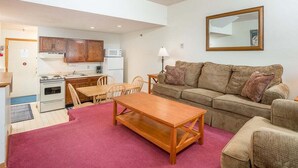 A compact living space with a kitchenette, a sofa, a wooden table, and a dining area. - Ski-In/Ski-Out Sunday River Condo: Sunrise A-120 (Newry)