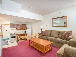 A compact living space with a kitchenette, a sofa, a wooden table, and a dining area. - Ski-In/Ski-Out Sunday River Condo: Sunrise A-120 (Newry)
