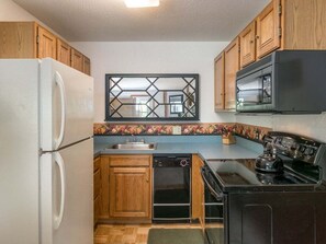 A compact kitchen with wooden cabinets, a white refrigerator, a dishwasher, a stove, and a microwave.