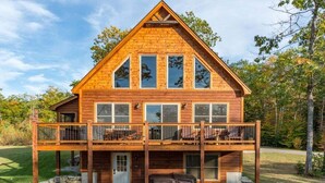 A wooden cabin with a balcony, a hot tub, and a stone foundation.