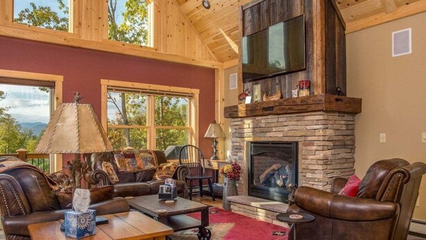 A spacious living room with a stone fireplace, leather furniture, and large windows.