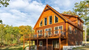 A two-story log cabin with a balcony, a hot tub, and a stone foundation.