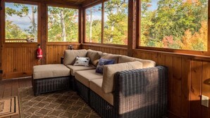 A covered outdoor seating area with a sectional sofa, a wicker chair, and a fire extinguisher.