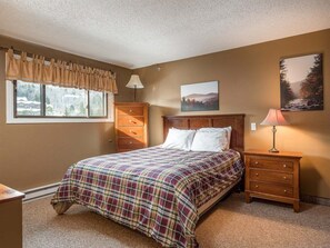 Un dormitorio con cama, cómoda, mesita de noche, ventana con cortinas y un cuadro en la pared.