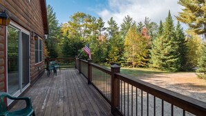 Une terrasse en bois avec une rambarde, un drapeau et une vue sur les arbres.