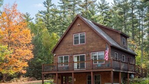 Une cabane en rondins à deux étages, dotée d’un balcon et d’une véranda, entourée d’arbres.