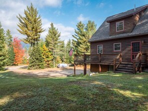 Une cabane en rondins avec une terrasse, entourée d’arbres et sous un ciel dégagé.