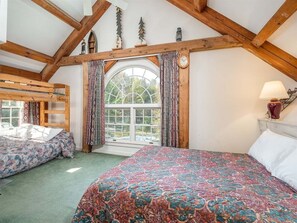 A bedroom with a large bed, a smaller bed, a window with curtains, wooden beams, and a lamp. - Riverbend 41: Two bedroom Condo (Bethel)