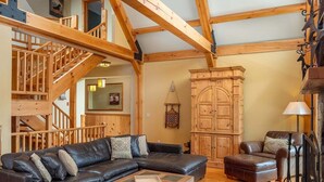 A spacious living area with a wooden staircase, a large L-shaped black leather sofa, a wooden coffee table, and a traditional wooden cabinet. - Powder Ridge Mountain Retreat (Newry)