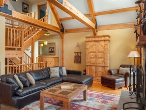 Ein geräumiger Wohnbereich mit einer Holztreppe, einem großen, L-förmigen schwarzen Ledersofa, einem Holztisch und einem traditionellen Holzschrank.