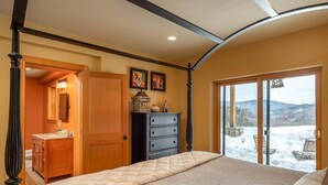 A bedroom with a four-poster bed, a dresser, a vanity, and a view of a snowy landscape through a glass door. - Powder Ridge Mountain Retreat (Newry)