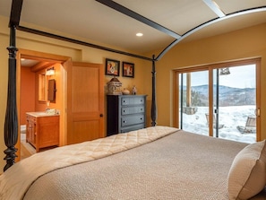 A bedroom with a four-poster bed, a dresser, a vanity, and a view of a snowy landscape through a glass door. - Powder Ridge Mountain Retreat (Newry)