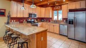 A kitchen with wooden cabinets, a granite countertop, a stainless steel refrigerator, and a bar stool area. - Powder Ridge Mountain Retreat (Newry)