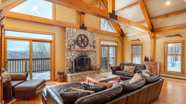 A spacious living room with a stone fireplace, leather sofas, and large windows. - Powder Ridge Mountain Retreat (Newry)