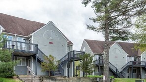 Una hilera de casas adosadas con escaleras exteriores, un jardín delantero con césped y un cielo nublado.