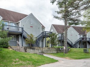 Una hilera de casas adosadas con escaleras exteriores, un jardín delantero con césped y un cielo nublado.