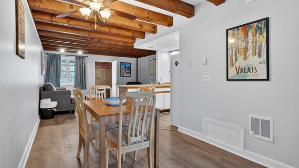 A dining area with wooden furniture, a ceiling fan, and a kitchen in the background. - Riverbend 29 - Post and Beam Condo (Bethel)