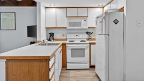 A modern kitchen with white cabinetry, a built-in microwave, a stove, and a refrigerator. - Riverbend 29 - Post and Beam Condo (Bethel)