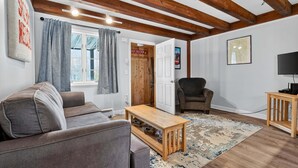 A living room with a sofa, a wooden coffee table, a TV stand, and a door leading to a bathroom.