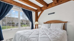A bedroom with a large bed, a window with curtains, a wooden ceiling, and a sign on the wall. - Riverbend 29 - Post and Beam Condo (Bethel)