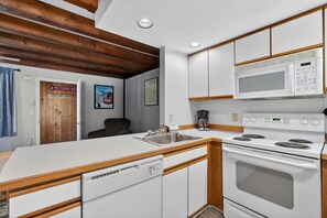 Une cuisine compacte équipée d’un lave-vaisselle, d’une cuisinière, d’un four à micro-ondes et agrémentée d’éléments décoratifs en bois.