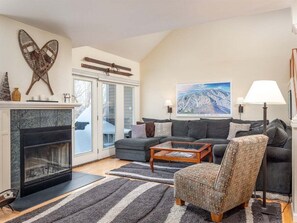A living room with a fireplace, a sofa, a patterned armchair, and a painting of a mountain landscape.