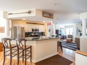 A modern kitchen with white cabinets, stainless steel appliances, and a bar area.