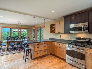 Uma cozinha moderna com armários de madeira, fogão de aço inoxidável e área de jantar com mesa e cadeiras.