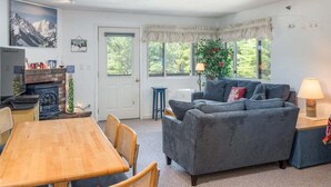 A cozy living room with a fireplace, a dining table, and a sofa. - Sunday River Condo: Brookside I B-306 (Newry)