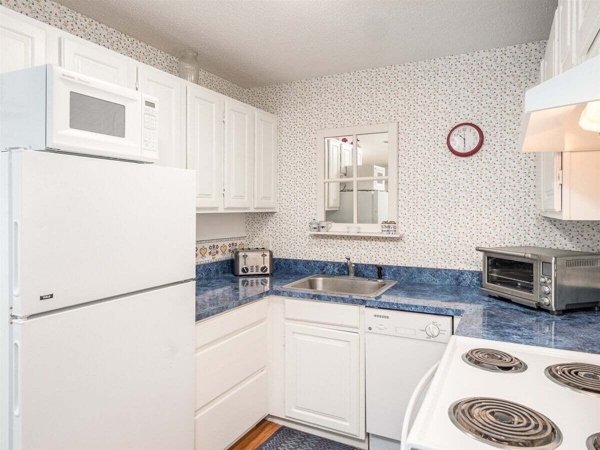 A compact kitchen with white cabinets, a microwave, a toaster, a sink, and a stove.