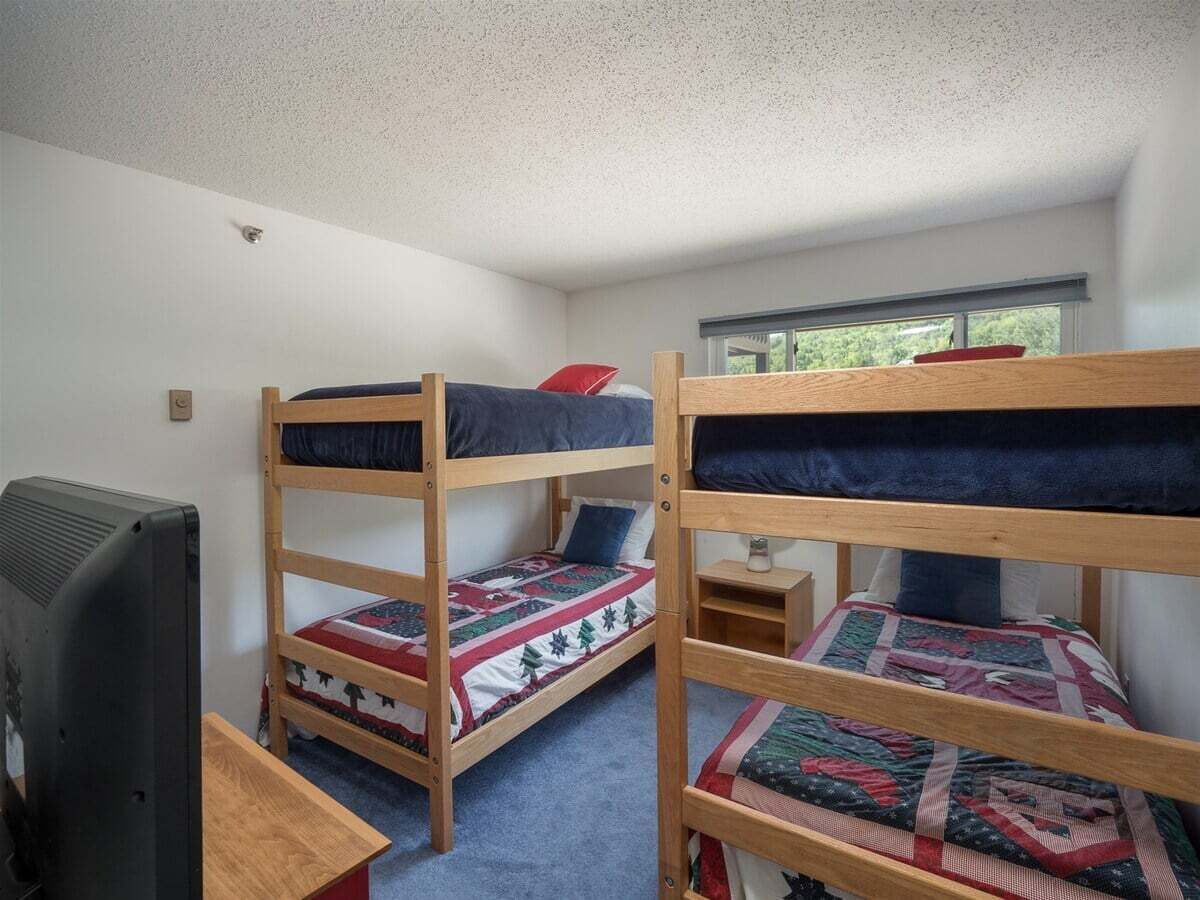 A dormitory room with bunk beds, a television, and a window with a view.