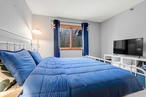 A room with a bed, a TV, a window with curtains, and a lamp.