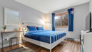Un dormitorio con cama, escritorio, silla y ventana con cortinas.