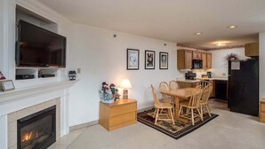 Uma sala de estar com lareira, televisão e um espaço de jantar com cadeiras e mesa de madeira.