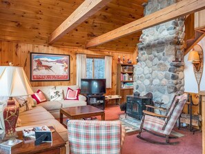 A cozy log cabin interior with a stone fireplace, wooden furniture, and a television.