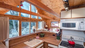 Cozinha estilo cabana com vigas de madeira, fogão, micro-ondas e uma janela grande com vista para uma paisagem nevada.