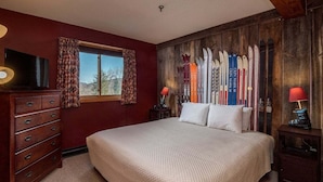 A bedroom with a large bed, wooden walls, a dresser, and skis on the wall. - White Cap A-104 - Sunday River Condo (Newry)