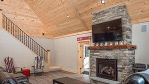 Ein Wohnzimmer mit Kamin aus Stein, Ledersofas, einer Holztreppe und einem Skiständer.