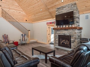 A living room with a stone fireplace, leather sofas, a wooden staircase, and a ski rack.