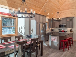 A modern kitchen with wooden ceiling, stainless steel appliances, and a dining area with a central island.