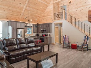 A spacious living area with a leather sofa, a dining table, and a kitchen in the background.