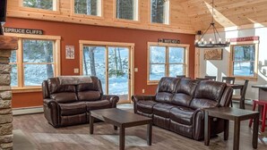 Ein geräumiges Zimmer mit Ledersofas, einem Holztisch und großen Fenstern mit Blick auf eine verschneite Landschaft.
